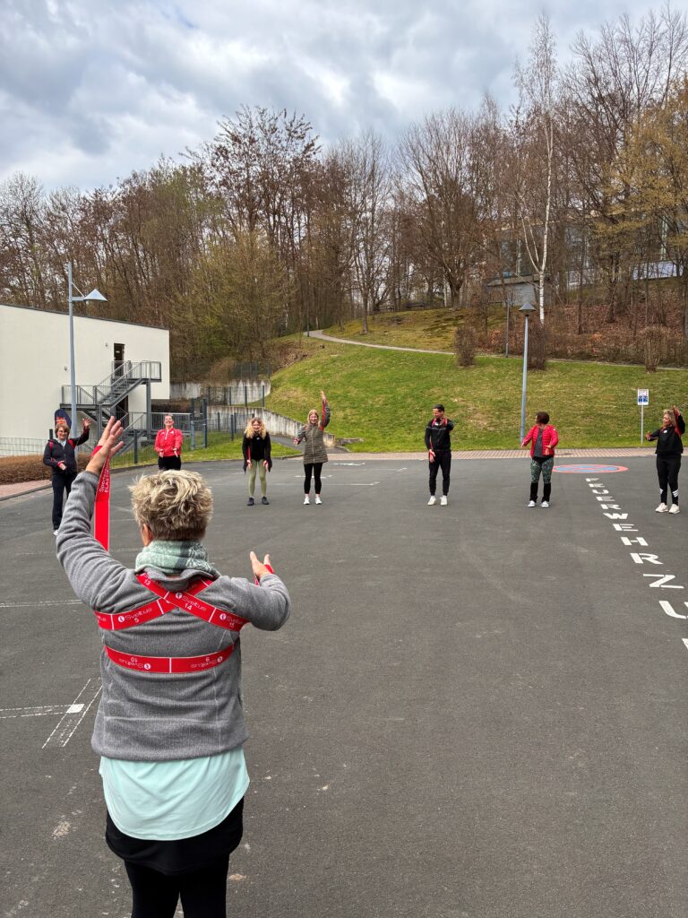Rückblick Netzwerktreffen März 2026: Der "bewegte Weg zur Achtsamkeit" im Rehasport 10 Outdoor Kreis mit Koerperband zur Aktivierung Schulterguertel Christiane von hinten - Rückblick Netzwerktreffen März 2026: Der "bewegte Weg zur Achtsamkeit" im Rehasport